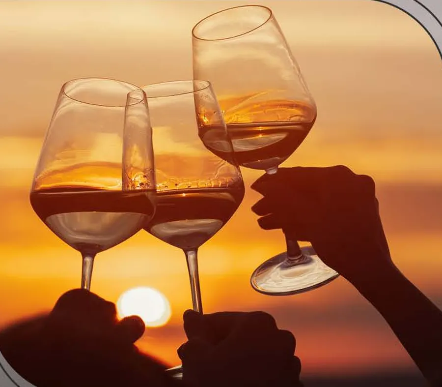 Três taças de vinho brindando contra o pôr do sol
