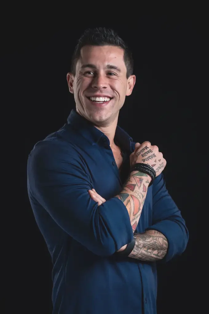 Johnny Destro with arms crossed, navy shirt, smiling, on a black background