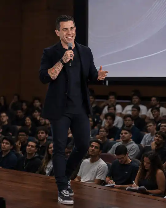 Johnny Destro palestrando de microfone em mãos num auditório universitário lotado
